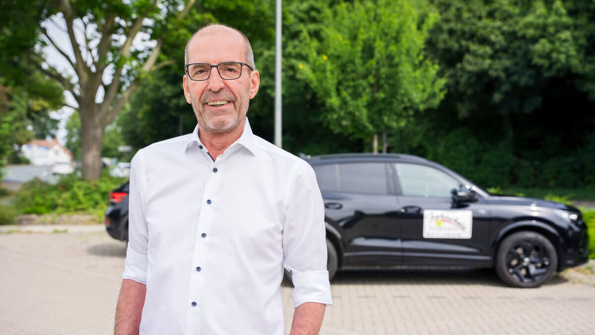 Portraitfoto Roger Koopmann mit Fahrschulauto im Hintergrund